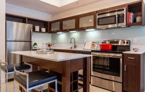 Luxury Apartments in Orlando, FL, with In-Unit Washer and Dryer - NORA - Kitchen with a Moveable Island, Bar Stools, White Quartz Countertops, Dark Wood Cabinetry, and Stainless Steel Appliances.