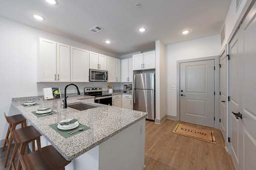 Huntsville, AL Luxury Apartments - The Kelvin - Kitchen with Luxury Vinyl Tile Flooring, Breakfast Bar with Seating, Granite Countertops, White Shaker-Style Cabinets, and Stainless-Steel Appliances.