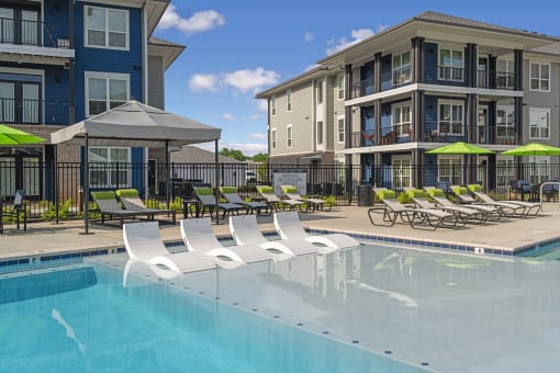 a swimming pool with lounge chairs and umbrellas in front of apartment buildings