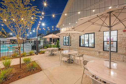 a patio with tables and umbrellas and a pool at night