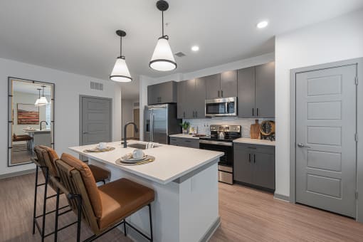 Studios in Chattanooga, TN - Populus Waterside - Kitchen with General Electric Stainless Steel Appliances, Quartz Countertops, Tile Backsplash, Kitchen Island/Breakfast Bar, Bar-Style Chairs, Pendant Lights, and Luxury Vinyl Tile Flooring.