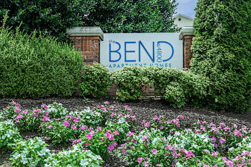A sign for Bend Apartment Homes is surrounded by flowers.