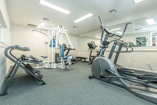 A gym with a variety of equipment including a treadmill, stationary bike, and weight bench.