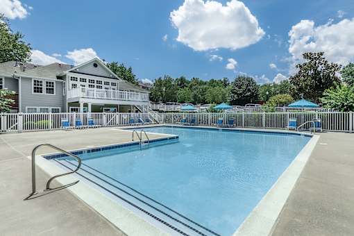 A large swimming pool in front of a house with a fence around it.