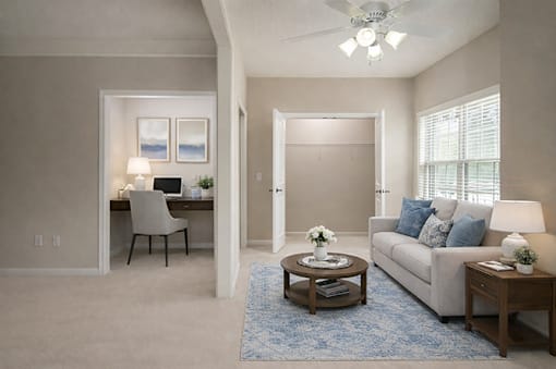A living room with a couch, a desk, and a ceiling fan.