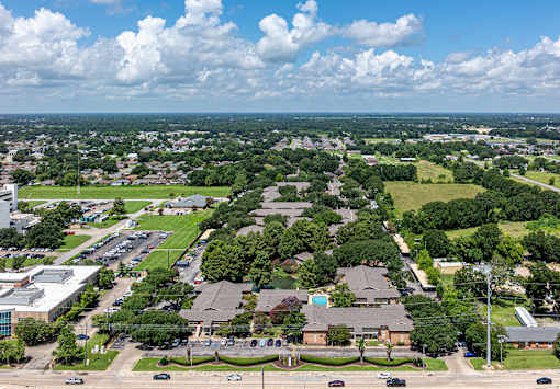 A bird's eye view of a residential area with houses, trees, and a parking lot.