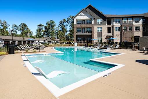 Cumming, GA, Luxury Apartments Near Alpharetta - Aura Creekside - Swimming Pool With In-Water Loungers, Pool Deck Seating, And Modern Apartment Buildings.