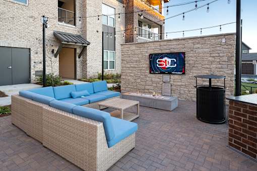 A patio with a couch and a TV on a stone wall.