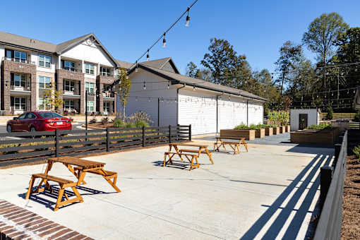 A sunny day at a park with picnic tables and a red car parked in the background.