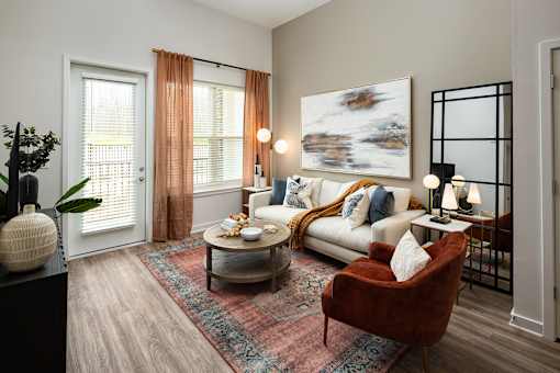 High-End Apartments in Cumming, GA - Aura Creekside - A Living Room With White Sofa, Rust Accent Chair, And A Round Coffee Table on a Patterned Rug.