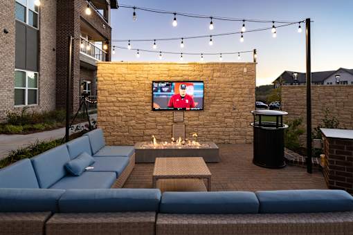 A patio with a blue couch and a television on a stone wall.