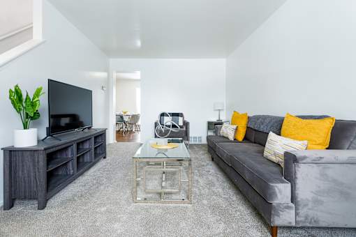 A living room with a grey couch and a glass coffee table.