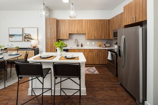 Decatur, GA, Apartments Near Marta Station - Arlo - Living Room With Black Sofa, Round Wood Coffee Table, Wall-Mounted Television, Dining Area, And Modern Kitchen In The Background.