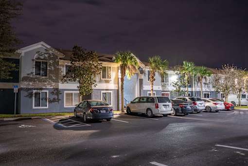 A parking lot with cars and a building with lights on in the background.