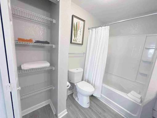 A white bathroom with a toilet, a tub, and a refrigerator.