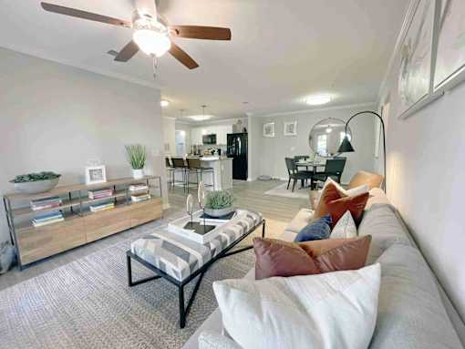 Greenville, SC Luxury Apartments With In-Unit Washer And Dryer - The Aventine Greenville - A Living Room And Dining Area With A Grey Sofa, Pillows, Wood-Style Flooring, And A View Into A Kitchen.