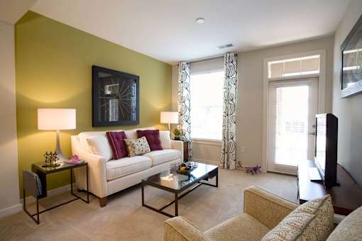 Charlotte, NC, Pet-Friendly Apartments - Gramercy Square at Ayrsley - Living Area with Couch, Armchair, Side Tables, Lamps, Coffee Table, Framed Decor, TV, Glass Door, and Large Window.