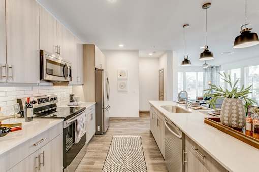 Luxury Apartments in Fort Worth, TX, with In-Unit Washer and Dryer - The Union at River East - Kitchen with Breakfast Bar, Quartz Countertops, Stainless Steel Appliances, and Pendant Lighting.