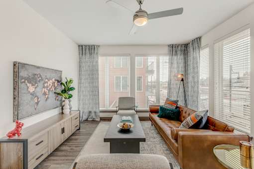 Fort Worth, TX, Luxury Apartments with In-Unit Washer and Dryer - The Union at River East - Living Room with a Brown Couch, Two Armchairs, Long Coffee Table, Cabinet, Ceiling Fan, and Floor Lamp.