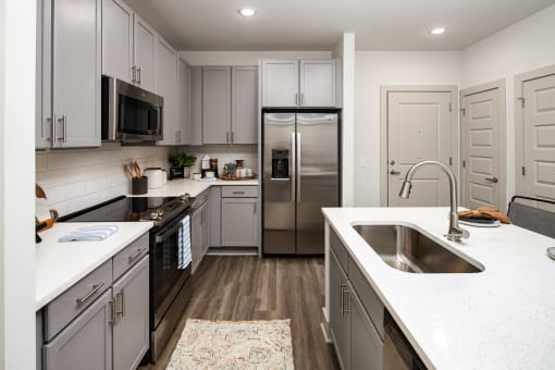 Apartments in Belmont, NC - The Banks Apartments - Gourmet Kitchen with Wood-Inspired Plank Flooring, Stainless-Steel Appliances, Quartz Countertops, Subway Tile Backsplash, and Grey Cabinets.