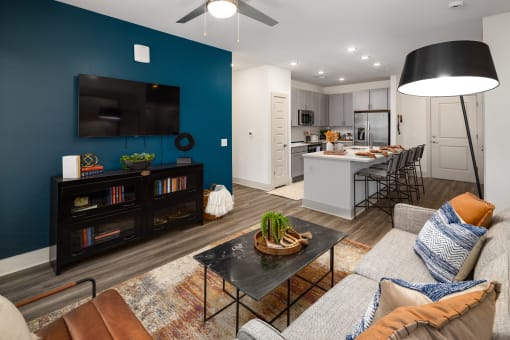 Apartments in Belmont for Rent - Banks at Mt. Holly - Open-Concept Living Room with Wood-Inspired Plank Flooring, Area Rug, Couch, Coffeetable, Floor Lamp, Wooden Media Consule, Ceiling Fan, and Access to Kitchen Area