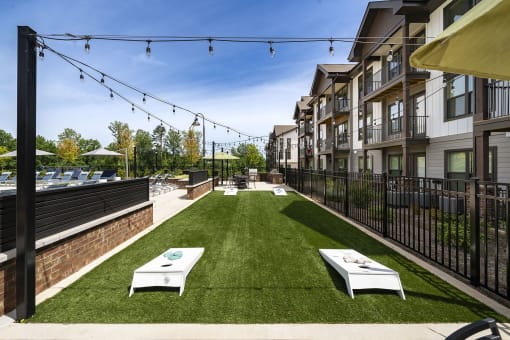 a grassy courtyard with two white tables and a fence