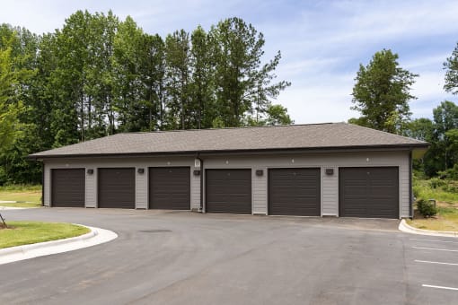 Apartments in Belmont, NC, for Rent - The Banks Apartments - Private Garages with Roll-Up Doors, Driveway, and Trees in the Background.