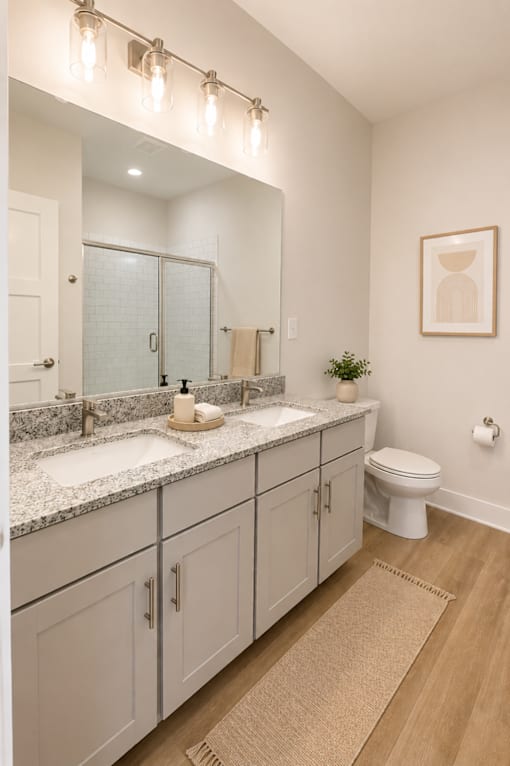A bathroom with a toilet, sink, mirror, and cabinetry.