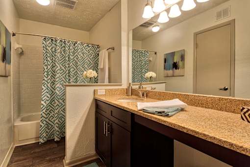 A bathroom with a patterned shower curtain and a sink with a brown counter top.