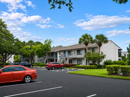 A red car is parked in a parking lot in front of a building.