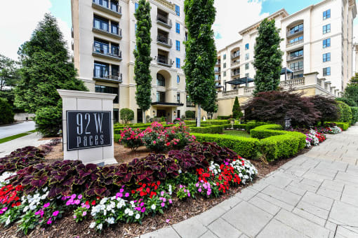 an apartment building with a sign and flowers in front of it