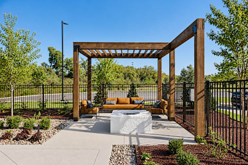 A wooden pergola with a bench and a fire pit in the middle of a garden.