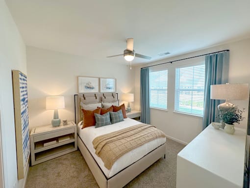 A bedroom with a large bed, a ceiling fan, and a window with blue curtains.