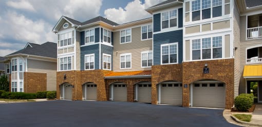 Luxury Apartments in Chapel Hill, NC, with In-Unit Washers and Dryers - The Reserve at Meadowmont - Property Exterior with Blue and Tan Walls, Stone Details, White Trim, Beige Attached Garages, Large Windows, and Manicured Hedges.