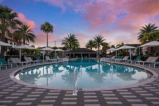 A round swimming pool surrounded by lounge chairs and palm trees.