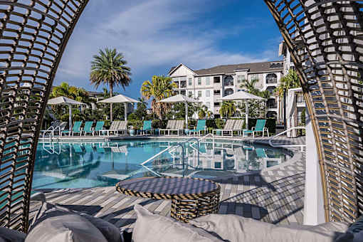 A pool surrounded by lounge chairs and umbrellas with a building in the background.