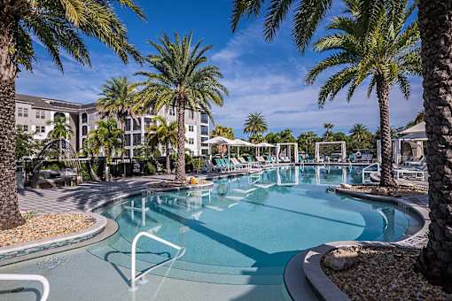 A pool surrounded by palm trees and a building in the background.