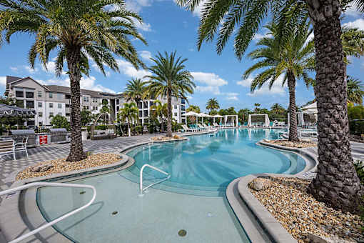 A pool surrounded by palm trees and a resort.
