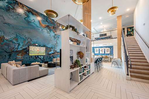 A living room with a large painting on the wall and a staircase on the right side.