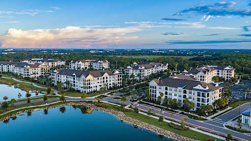 A large white building complex is surrounded by a lake and greenery.