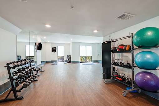 A gym with a variety of equipment including dumbbells, exercise balls, and a bench press.