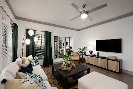 A living room with a white couch, a coffee table, a flat screen TV, and a ceiling fan.