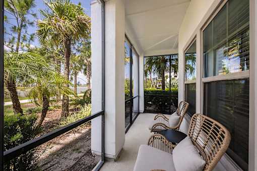 A balcony with white cushioned chairs and a table.