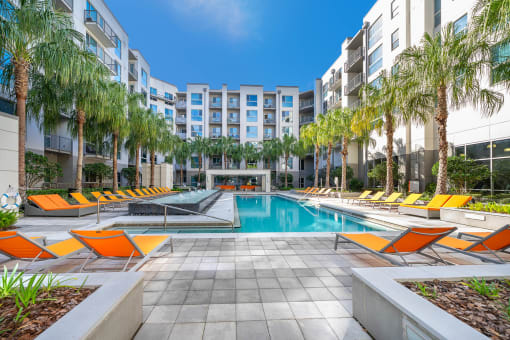 Orlando, FL Luxury Apartments Near Lake Eola Park - NORA - Resort-Style Pool with Spacious Sundeck, Vibrant Lounge Chairs, Planters, and Palm Trees.