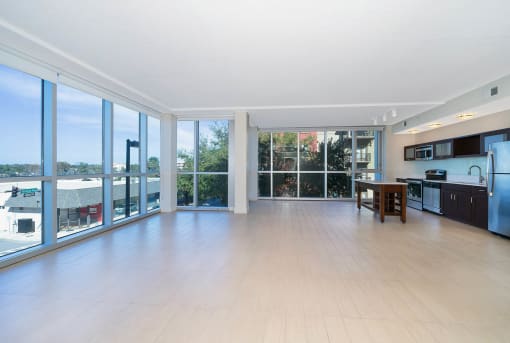 Orlando, FL, Luxury Apartments Near Lake Eola Park - NORA - An Empty Open-Concept Living Area with Wood-Style Flooring, Floor-to-Ceiling Windows with Roll-Up Blinds, and Adjacent to the Kitchen.