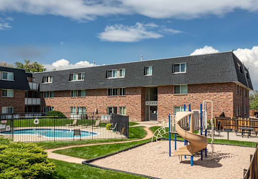 A playground with a slide and swimming pool in front of a brick building.