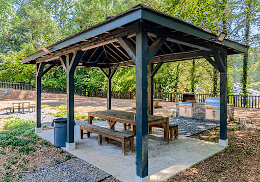 A wooden pavilion with a roof and four benches is situated in a park.