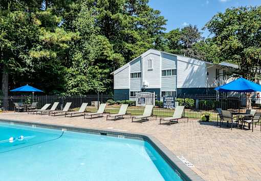 A pool with lounge chairs and umbrellas in front of a building.