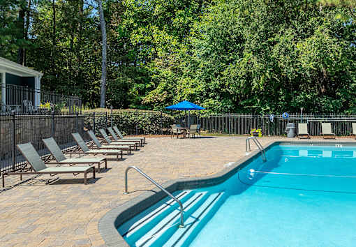 A pool surrounded by trees and chairs.