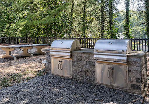 Three outdoor grills are lined up on a gravel area.